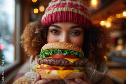 Young happy chubby woman with big cheeseburger having lunch in cafeteria  smiling girl portrait close-up