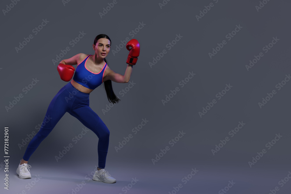 Beautiful woman wearing boxing gloves in color lights on grey background. Space for text