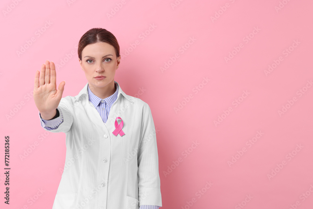 Mammologist with pink ribbon showing stop gesture against color background, space for text. Breast cancer awareness Mammologist with pink ribbon showing stop gesture against color background, space for text. Breast cancer awareness