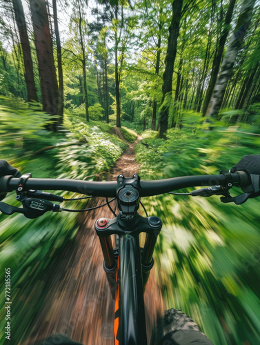 A person is riding a bike through a forest. The bike is black and the rider is wearing black gloves. The rider is looking ahead, possibly at the path ahead or at the trees. The forest is lush