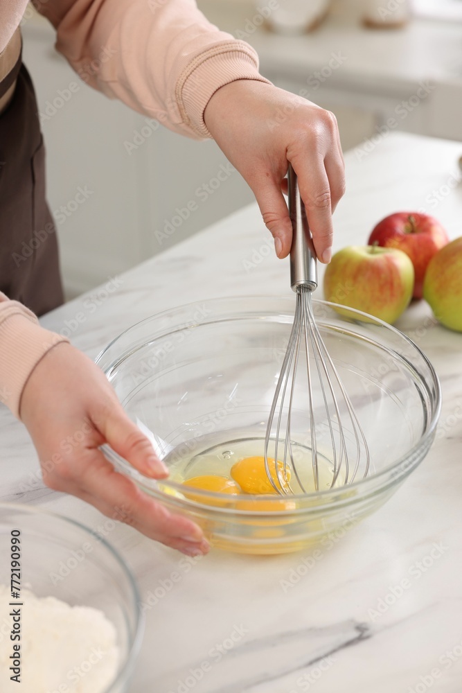 Woman whisking eggs in bowl at light marble table indoors, closeup Woman whisking eggs in bowl at light marble table indoors, closeup