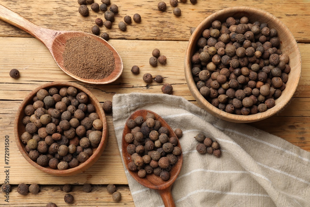 Aromatic allspice pepper grains in bowls, powder and spoons on wooden table, flat lay Aromatic allspice pepper grains in bowls, powder and spoons on wooden table, flat lay