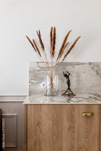 Twig plant in a hardwood vase on wooden cabinetry next to a statue