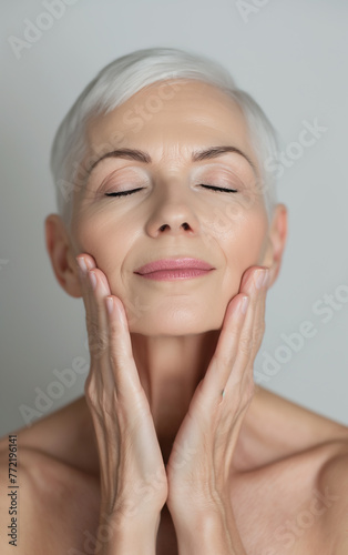 A close-up of a happy middle age beautiful elderly gray hair senior woman smiling and touching her face. Face skin care beauty. Advertising facial anti-age.