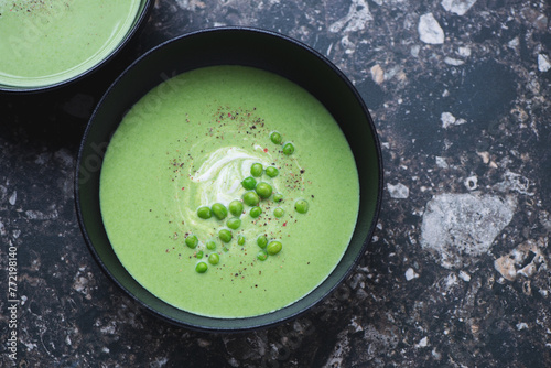 Black bowl with green pea cream-soup on a dark-brown granite background, horizontal shot with space, above view