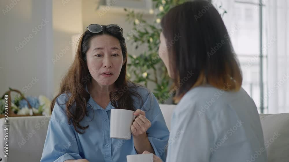 Two Asian Middle aged woman drinking coffee and having fun talking about the past on couch at home.female friends have fun drinking coffee enjoy in living room.Reunion,reunification,childhood friend Two Asian Middle aged woman drinking coffee and having fun talking about the past on couch at home.female friends have fun drinking coffee enjoy in living room.Reunion,reunification,childhood friend