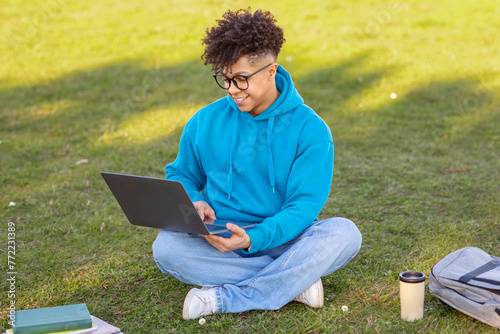 Male student working on laptop in grassy field photo