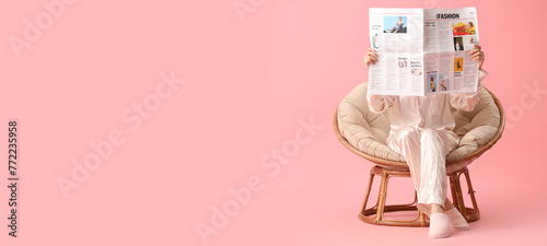Young woman reading newspaper in armchair on pink background