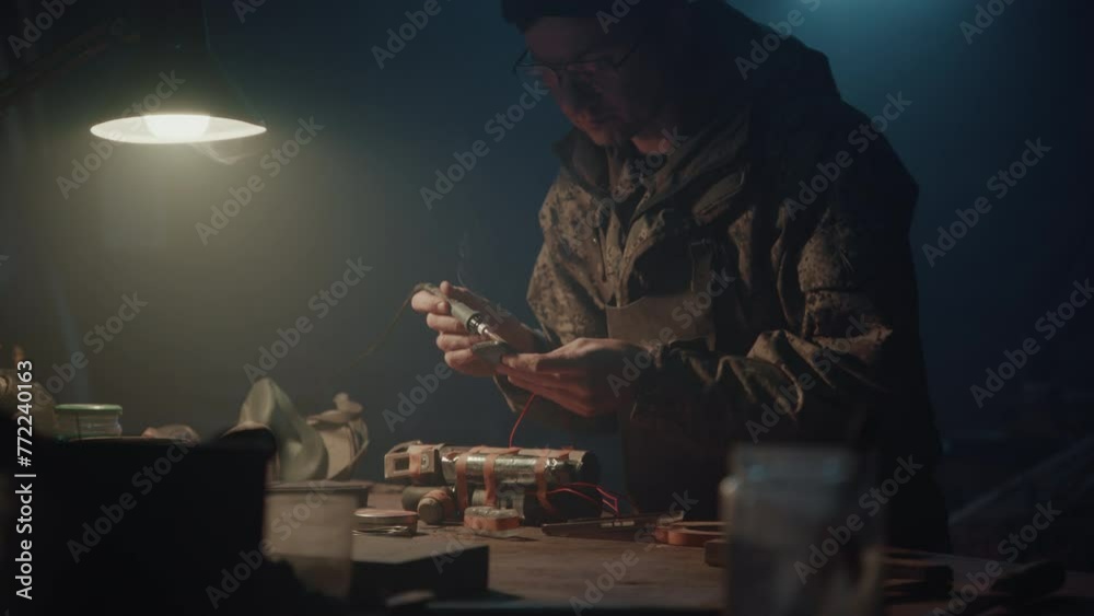 A man solders the phone to a home-made bomb in his workshop at night A man solders the phone to a home-made bomb in his workshop at night