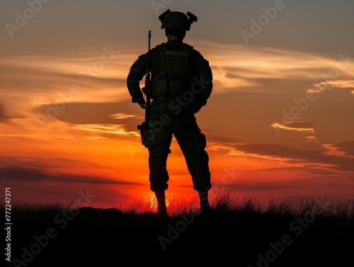 A man in a military uniform stands in the grass at sunset. He is holding a rifle and he is waiting for something