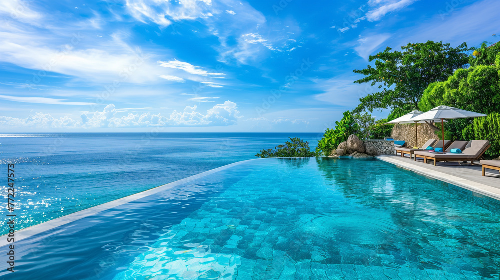 A tranquil infinity pool overlooking the ocean with sun loungers and palm trees against a clear sky..