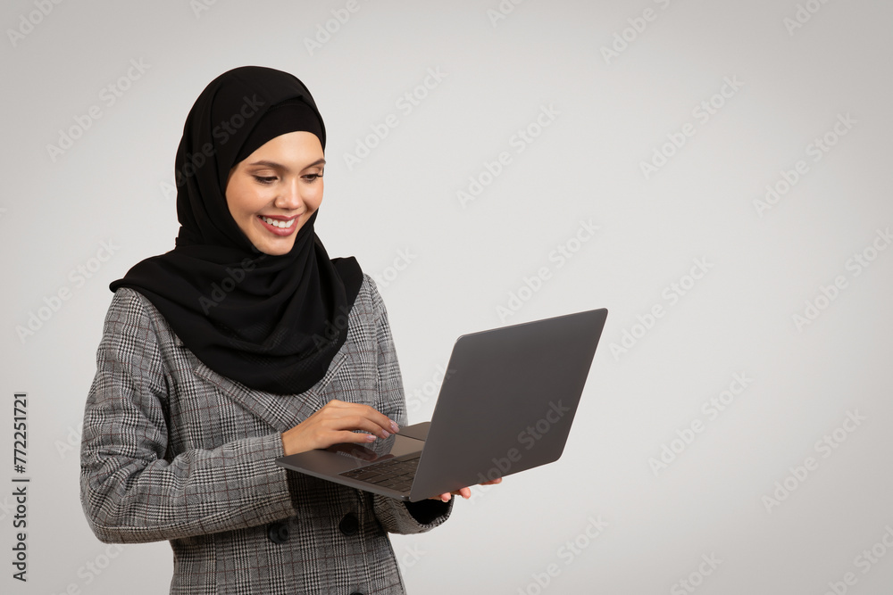 Smiling Muslim woman working on laptop, copy space Smiling Muslim woman working on laptop, copy space
