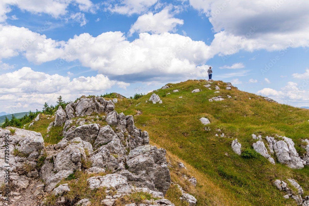 Person stands on a green hilltop against the backdrop of a blue cloudy sky. Big Fatra, Slovakia.
