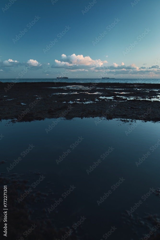 Fototapeta premium Sunset reflecting clouds on the ocean's surface seen from a beach vantage point