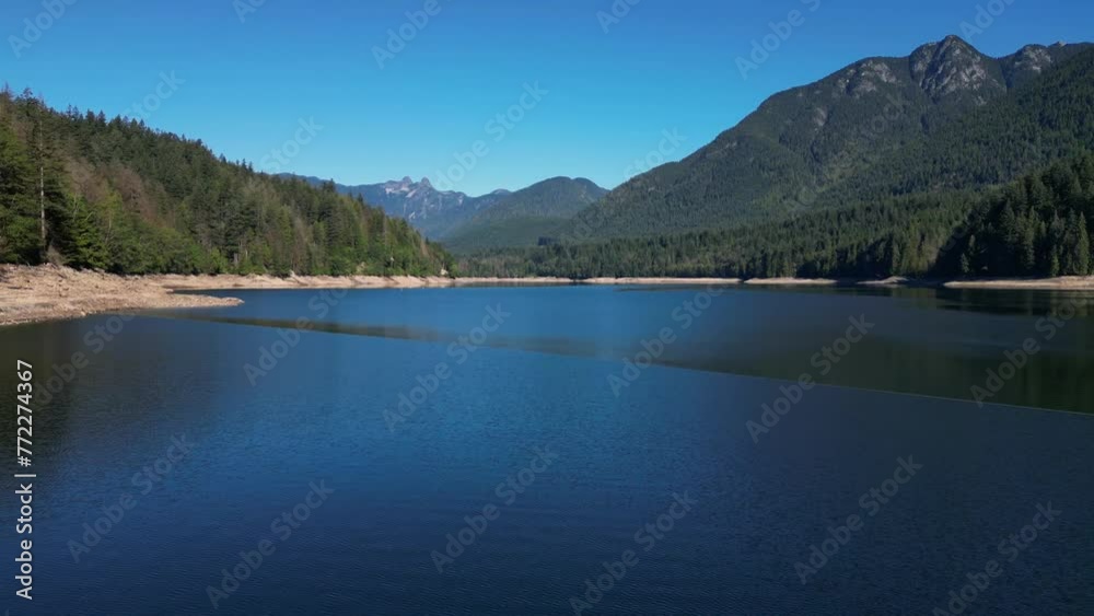 Aerial of a calm lake surrounded by forests and mountains on a sunny day Aerial of a calm lake surrounded by forests and mountains on a sunny day