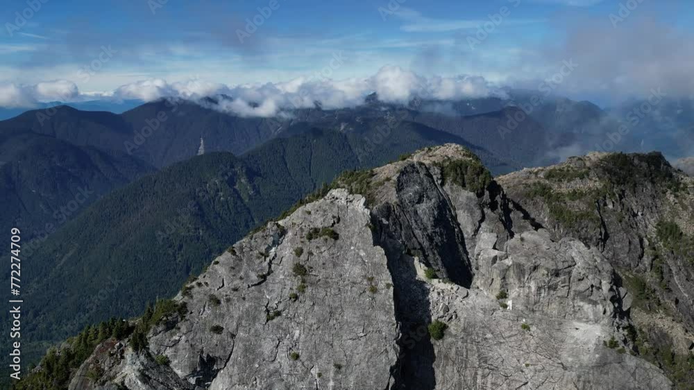 Aerial of big mountains covered in green forests with low clouds on a sunny day Aerial of big mountains covered in green forests with low clouds on a sunny day