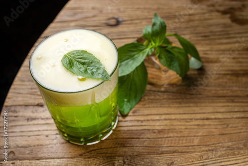 A glass of green alcoholic cocktail with basil on a wooden table.