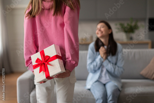 Daughter making surprise and hiding gift box for her excited mother, congratulating with birthday, enjoying family festivity © Home-stock