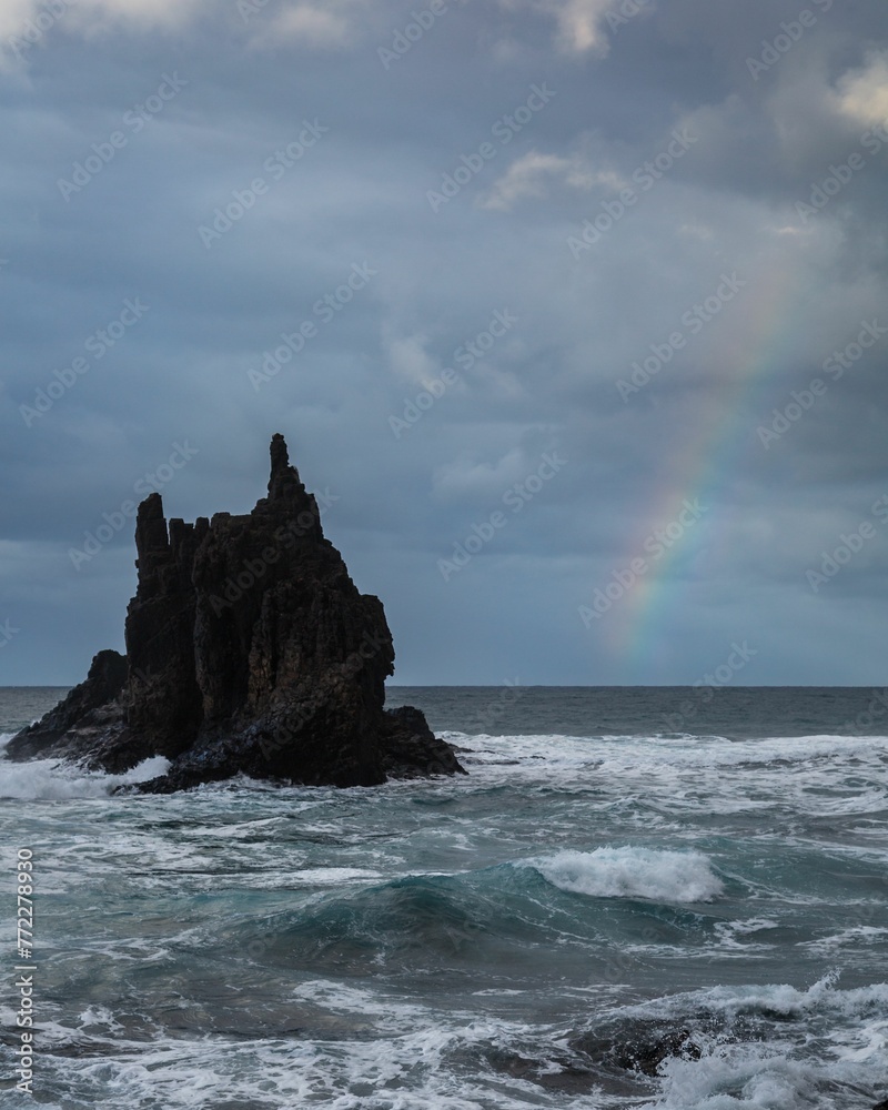 Beautiful rainbow arches over a tranquil ocean landscape with jagged rocks jutting out of the waters