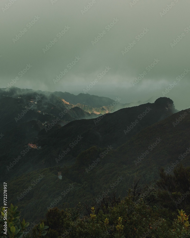 Scenic landscape of rolling green hills set against a backdrop of cloudy, misty mountains