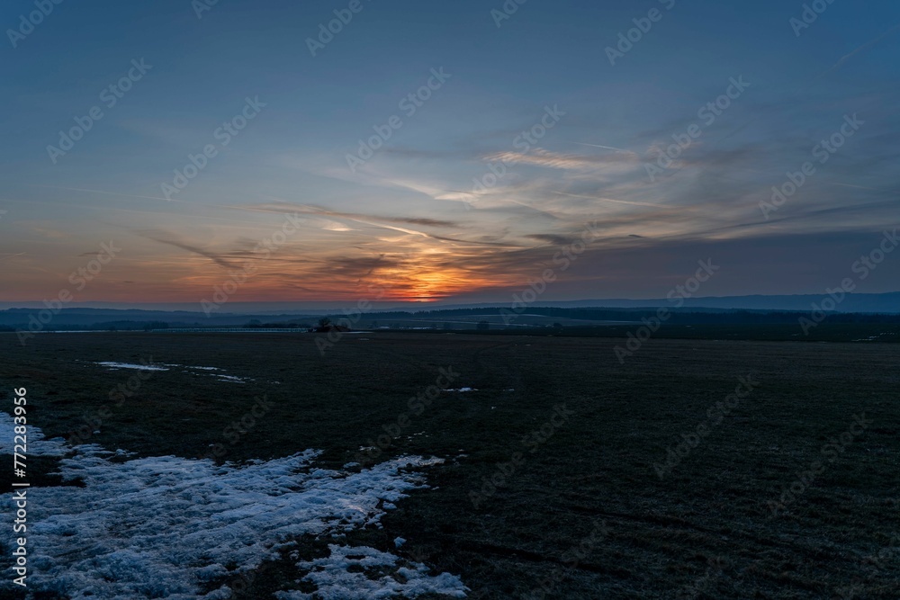 the sun is setting over a snow covered field with patches of grass