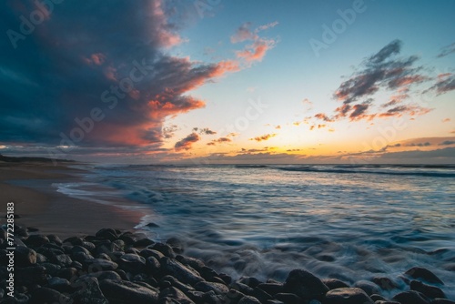 Scenic beach landscape with turbulent waves crashing against the shore against the cloudy sunset sky