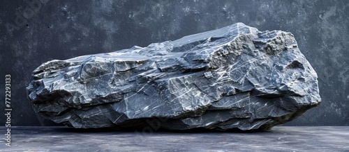 A sizeable gray rock resting on top of a concrete floor, contrasting textures between the rough surface of the rock and the smooth finish of the floor.