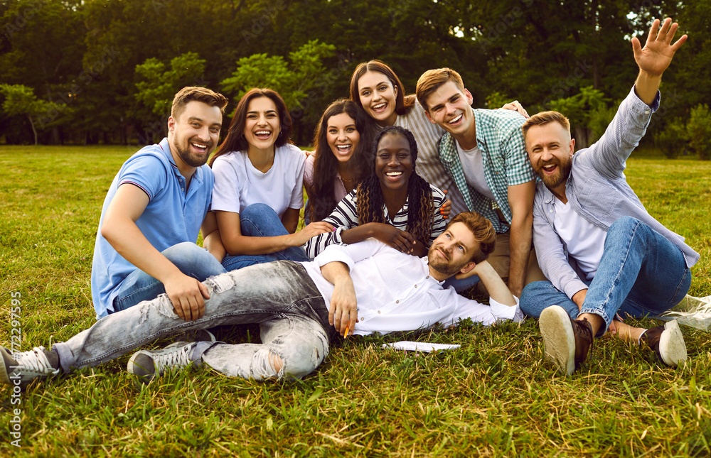 Fototapeta premium Happy diverse university students and friends having fun together. Team of cheerful muliracial young people posing for group photo portrait on green grass in park in summer