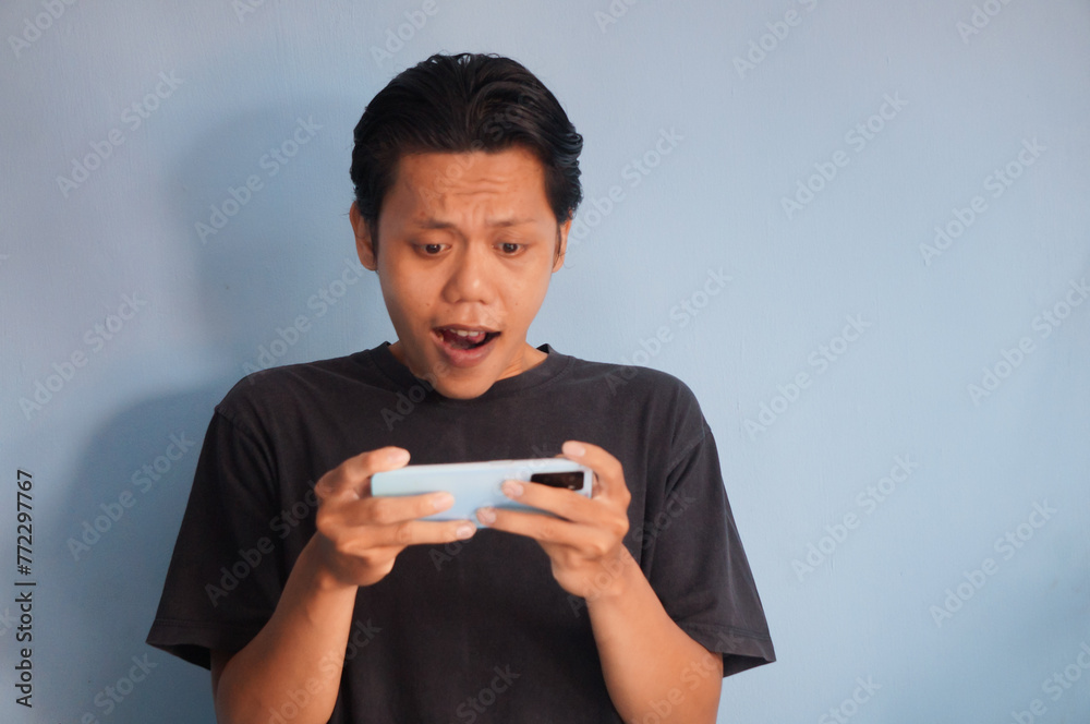 Excited young Asian man wearing black shirt playing game on smartphone isolated on white background Excited young Asian man wearing black shirt playing game on smartphone isolated on white background
