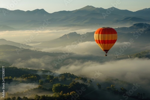 A hot air balloon is flying over foggy mountains high in air