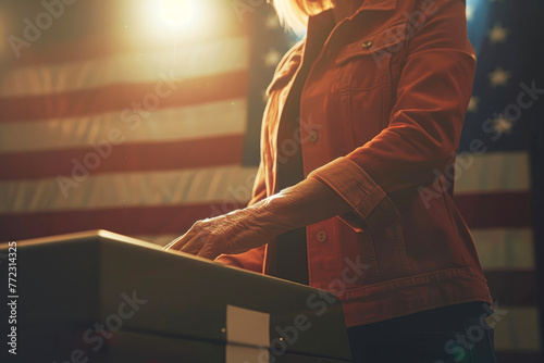 A woman in a red jacket is standing in front of a large American flag. She is holding a keyboard and she is typing