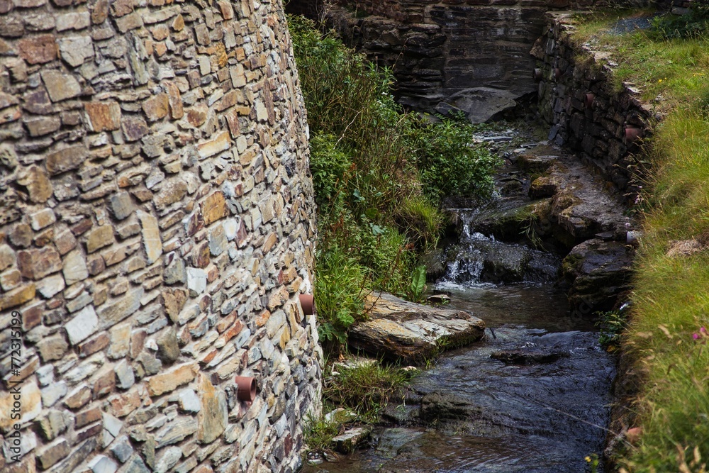 water flowing between two stone walls and grass at the edge