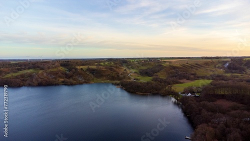 Scenic view of a tranquil lake surrounded by lush greenery at sunset. © Wirestock