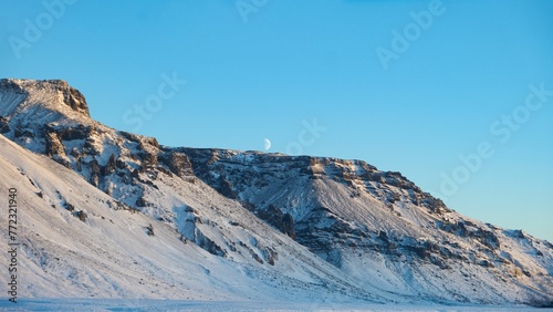 the moon is setting on a snowy mountain and sky as seen from the side © Wirestock