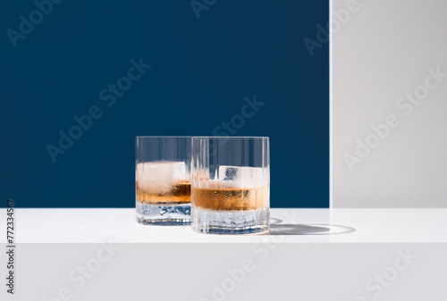 Dos vasos de whisky con hielo sobre un fondo azul	
