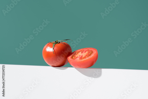 Un tomate maduro entero y cortado por la mitad sobre un soporte blanco y fondo verde photo