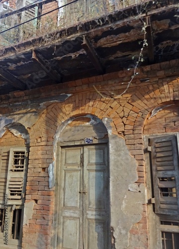 Neglected building facade showing weathered door and broken wooden window. © sumit