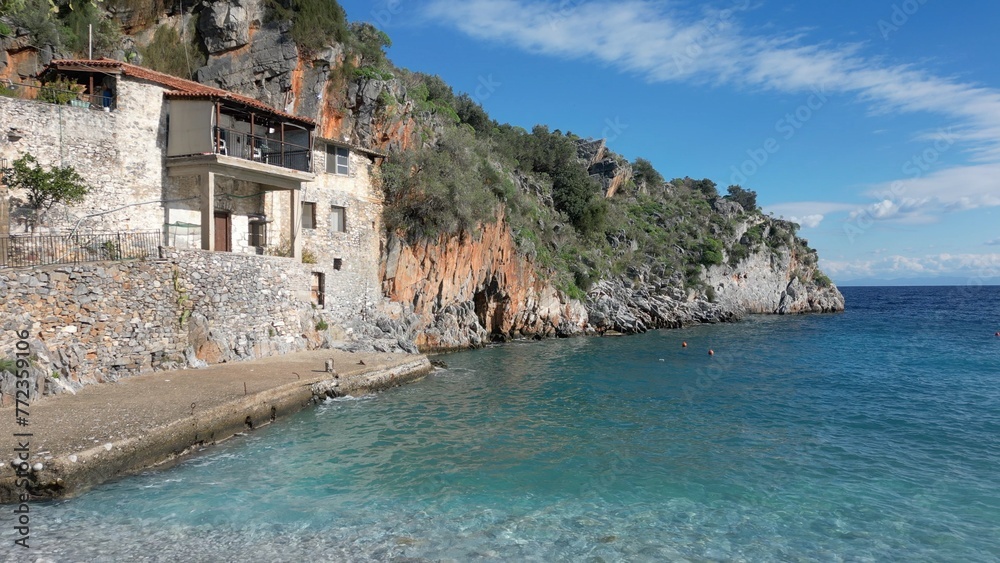 Alypa Beach, Mani Peninsula, Lakonia, Peloponnese, Greece, a beautiful stone beach with a transparent and turquoise sea water and cave in a cliff - drone aerial view