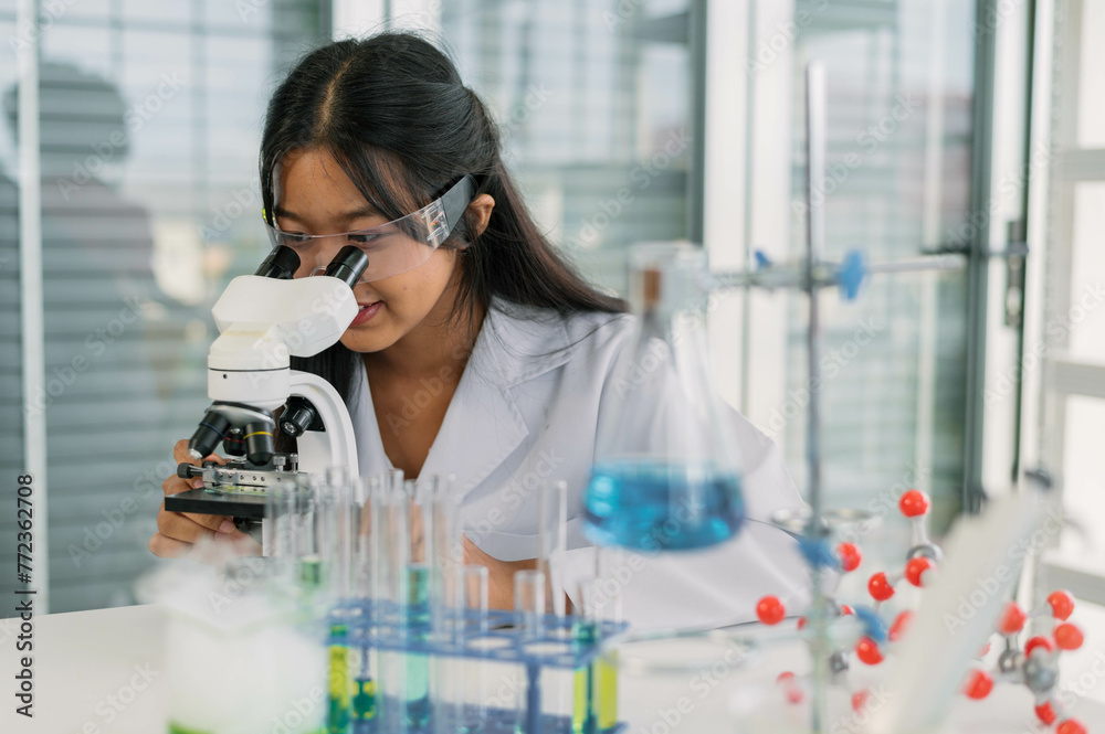 Professional woman scientist conducts research using a microscope among laboratory glassware. Professional woman scientist conducts research using a microscope among laboratory glassware.