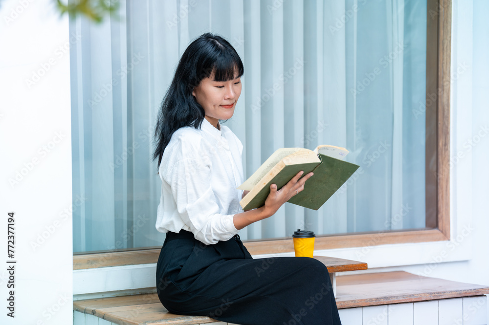 Asian women enjoy reading good books. Holding an open book and a cup of coffee on the table in a quiet cafe. Asian women enjoy reading good books. Holding an open book and a cup of coffee on the table in a quiet cafe.