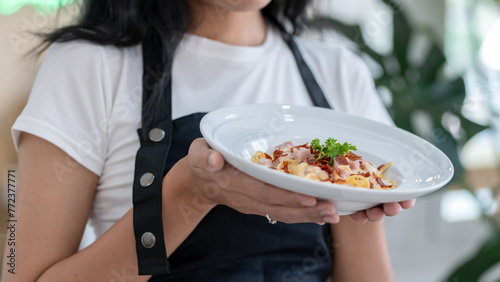 An Asian woman proudly wears an apron with a beautifully arranged plate of food ready to be served.