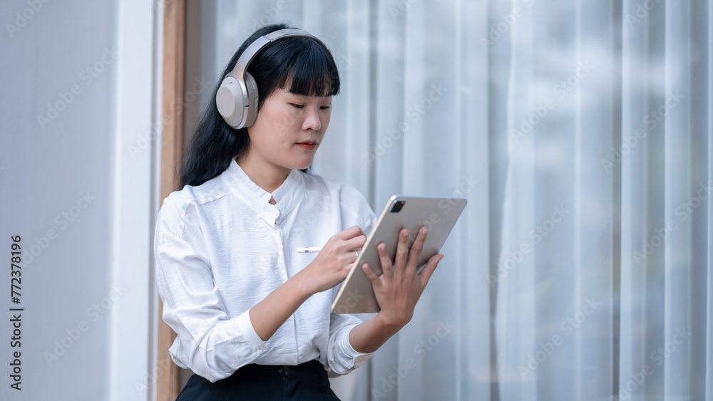 Blissful Asian woman with closed eyes savoring music on wireless headphones, holding a digital tablet. Blissful Asian woman with closed eyes savoring music on wireless headphones, holding a digital tablet.