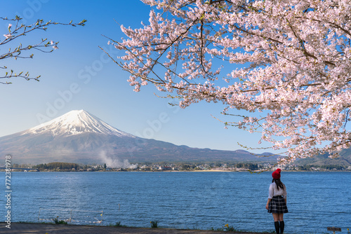 A woman in a Japanese student uniform admires Lake Kawaguchiko, beautifully framed by blooming cherry blossoms with mount Fuji on background