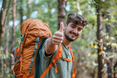 Happy smiling young man with thumbs up and color big backpack wearing forest background