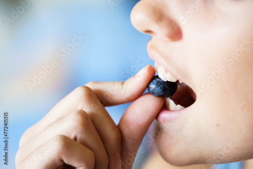 Anonymous young girl biting delicious organic blueberry at home