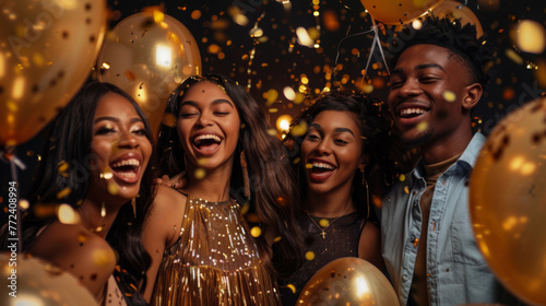 Exuberant friends laugh and celebrate with gold balloons and falling confetti.