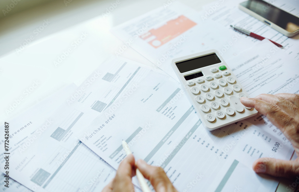 Close-up shot. business owner use calculator to manage financial documents bills invoices pay utilities calculate business commercial cost income and tax. checking purchese order from customer Close-up shot. business owner use calculator to manage financial documents bills invoices pay utilities calculate business commercial cost income and tax. checking purchese order from customer