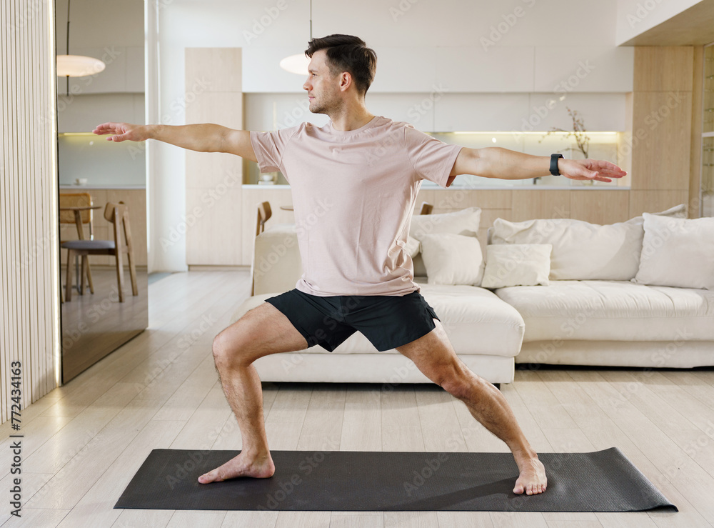 A man practices the Warrior II yoga pose with precision and calmness, harmonizing his body and mind in a well-lit, open home space. A man practices the Warrior II yoga pose with precision and calmness, harmonizing his body and mind in a well-lit, open home space.