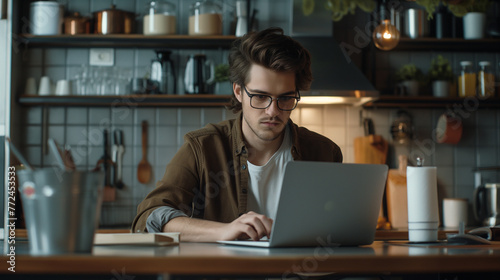 Focused young man wearing glasses using laptop, typing on keyboard, writing email or message, chatting, shopping, successful freelancer working online on computer.