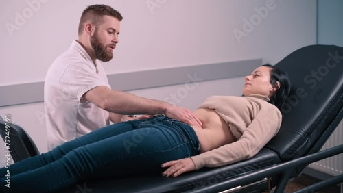 A doctor palpates the abdomen of a patient in the clinic. A young woman with abdominal pain lies on the couch. photo